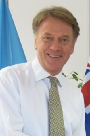 A middle aged white man smiling for the camera in a white shirt and green tie and brown hair